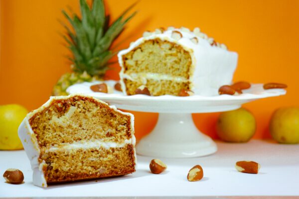Sliced pineapple and almond cake displayed on a cake stand with vibrant orange background.