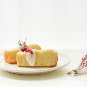 Slice of sponge cake with cream and berry topping on a white plate with floral garnish.