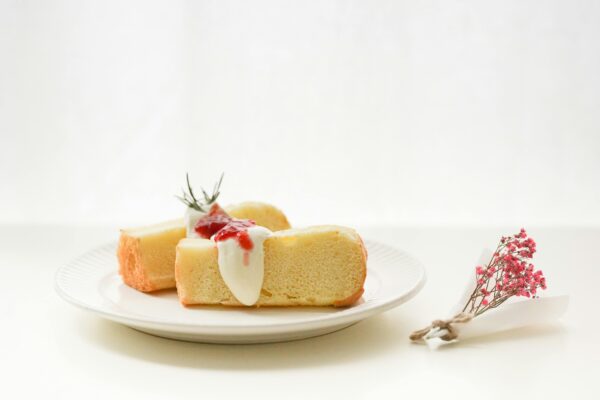 Slice of sponge cake with cream and berry topping on a white plate with floral garnish.