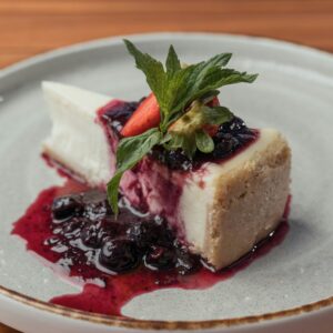 Slice of creamy cheesecake topped with blueberries and mint on a ceramic plate.