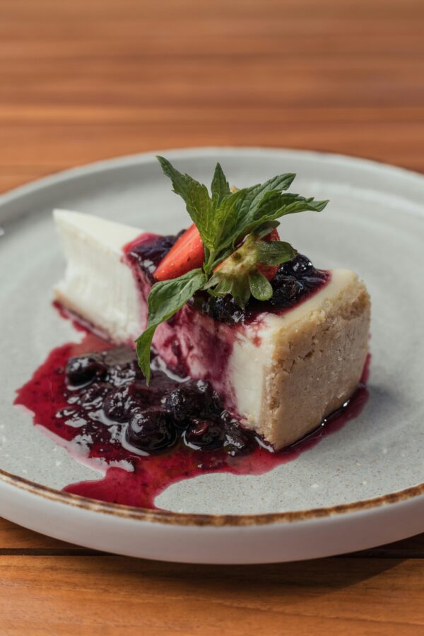 Slice of creamy cheesecake topped with blueberries and mint on a ceramic plate.