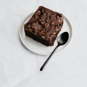 A delectable piece of chocolate cake with nuts on a white plate.