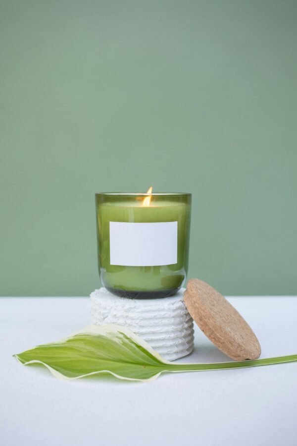 Minimalist candle with leaf on white surface, perfect for relaxation themes.